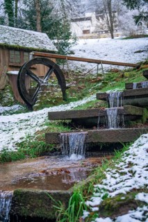 A small water wheel with a snow-covered stream in picturesque winter, spa garden, Bad Wildbad,