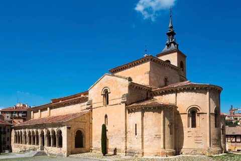 Historic church with stone arches and a Gothic tower under a blue sky, Church of San Millan,
