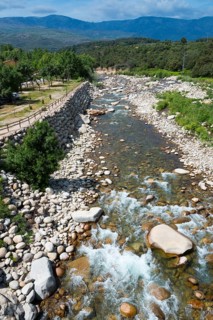 Wilder Fluss, der durch eine steinige Berglandschaft fließt, mit grünen Bäumen und Hügeln unter
