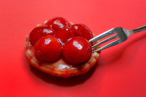 Strawberry tartlet with fork on red background, fruit cake