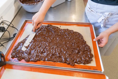 A person spreads and smoothes chocolate with a spatula on a baking mat, Burch Schokolade
