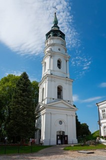 White baroque church tower with greenery in a picturesque setting under a blue sky, bell tower of