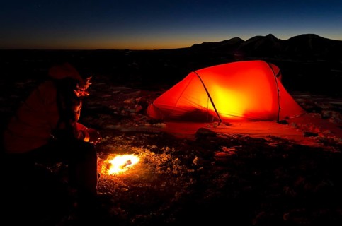 Man with campfire and lit tent, Engerdalsfjellet, Rendalssölen peak in the background, Hedmark