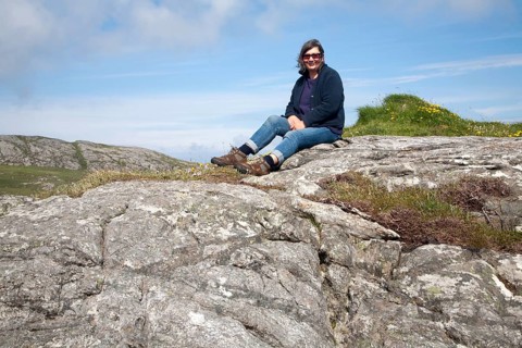 Middle aged female hiker sitting high on rocky outcrop in Barra, Outer Hebrides, Scotland, UK