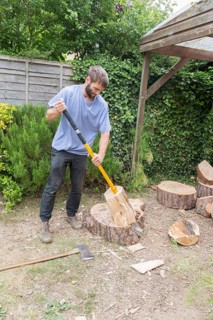 Young man using log splitter tool to split pine tree logs, Suffolk, England, UK