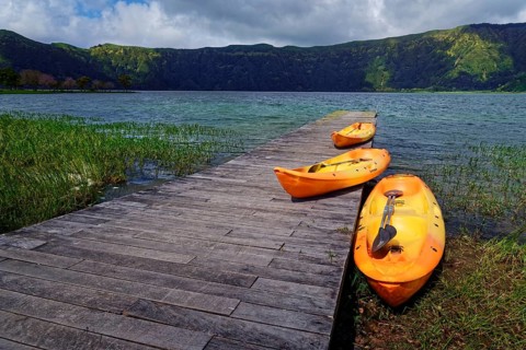 Three orange kayaks on the wooden jetty of the crater lake Lagoa Azul, surrounded by greenery and