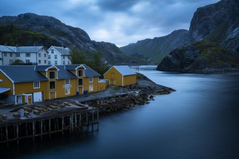 View of Nusfjord with yellow or ochre-coloured and white houses by the sea, mountains in the