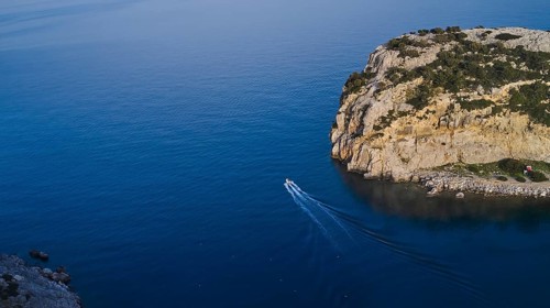 Drone shot, Small boat navigating through the clear blue water along a steep cliff, Anthony Quinn