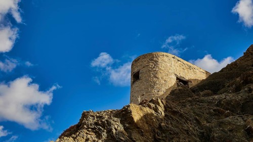 Ruin of a windmill, Stone tower on a rock, surrounded by blue sky and clouds, Colourful mountain