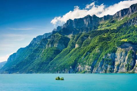 Sunny view over Lake Walen with the small chive island in the turquoise water and mountain range