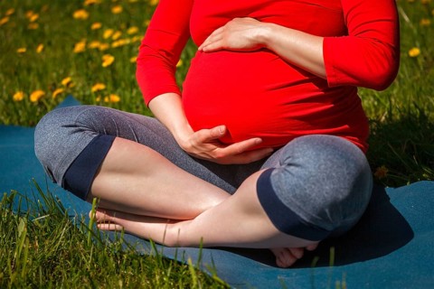 Pregnancy yoga exercise, pregnant woman doing asana Sukhasana easy yoga pose holding her abdomen