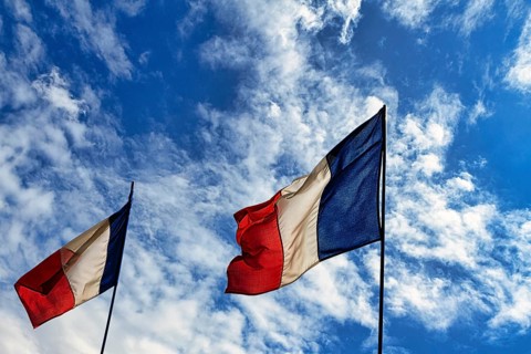 Two French national flags fluttering side by side in the wind, tricolour, slightly cloudy sky,