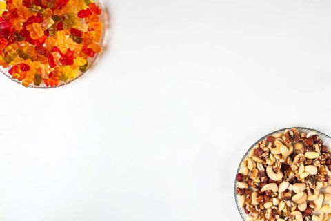 Comparison of unhealthy and healthy, gummy bears and various nuts, on plates, white background,