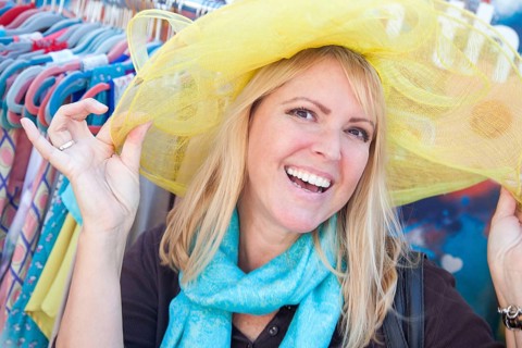 Happy blonde woman playfully modeling a big sun hat at the market