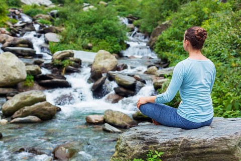 Woman doing yoga meditation asana Padmasana lotus pose outdoors at tropical waterfall