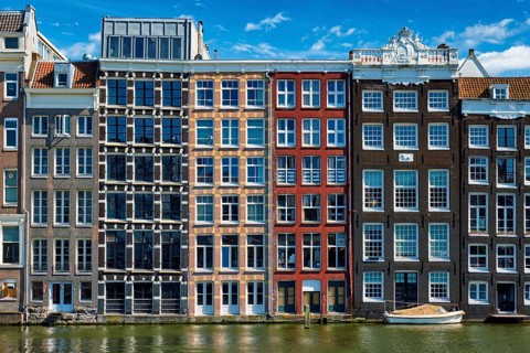 Row of typical houses and boat on Amsterdam canal Damrak with reflection. Amsterdam, Netherlands