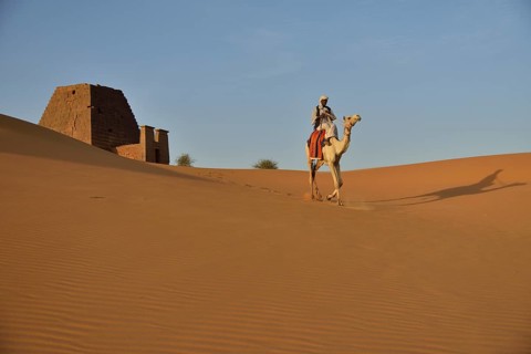 Man riding a dromedar in front of a pyramid of the northern cemetery of Meroe, Nubia, Nahr an-Nil,