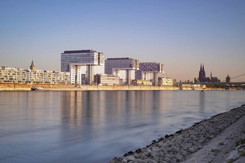 Crane houses in the Rheinau harbour and Cologne Cathedral seen across the Rhine from the bollard