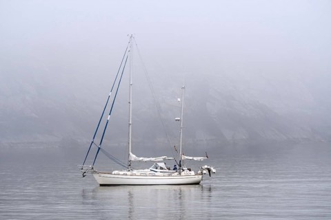 Sailboat, sailing boat, yacht with lowered sails at sea during bad visibility due to thick fog,