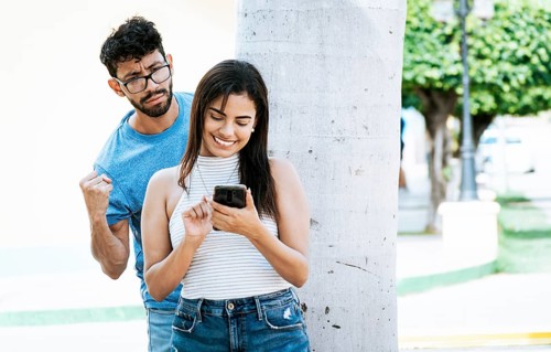 Jealous man spying on his girlfriend texting on the cell phone. Suspicious man spying on his