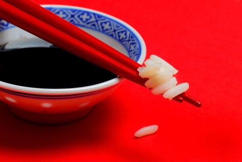 Rice grains on chopsticks, bowl with soy sauce, chopsticks, rice