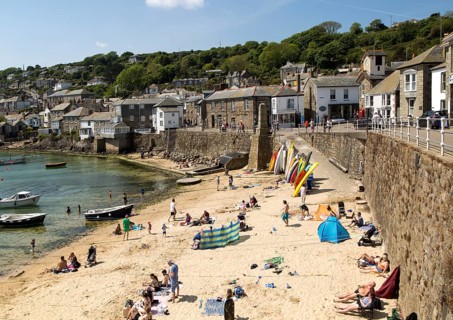 People on crowded beach in Mousehole village, Cornwall, England, UK