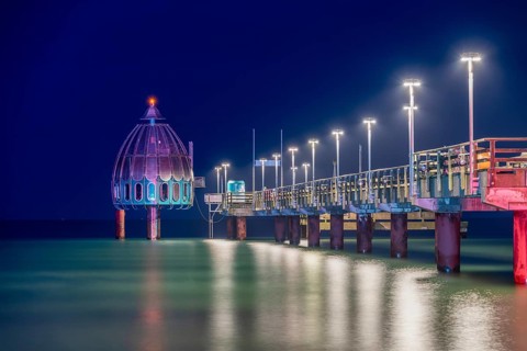 Diving gondola and long illuminated pier in the sea at night, calm water reflects lights, Zingst,