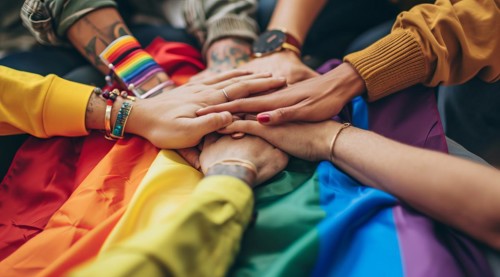 Diverse people hands over rainbow LGBTQ flag showing love, affection and unity, AI generated