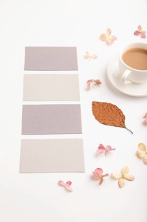 Composition with gray paper business card, brown beech autumn leaves, hydrangea flowers and cup of