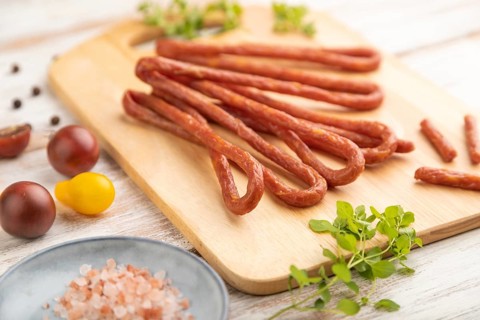 Traditional polish smoked pork sausage kabanos on cutting board with salt and pepper on white