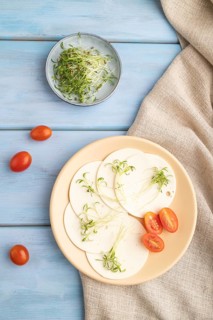 White cheese with tomatoes and cilantro microgreen on blue wooden background and linen textile. top