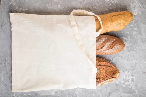 Reusable textile grocery bag with fresh baked bread on a gray concrete background. top view, flat