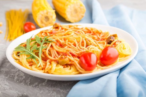 Corn noodles with tomato sauce and arugula on a gray concrete background and blue textile. Side