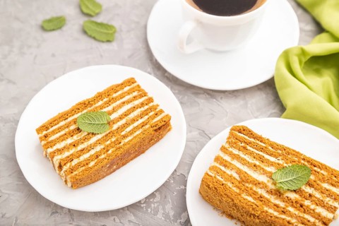 Homemade honey cake with milk cream and mint with cup of coffee on a gray concrete background and