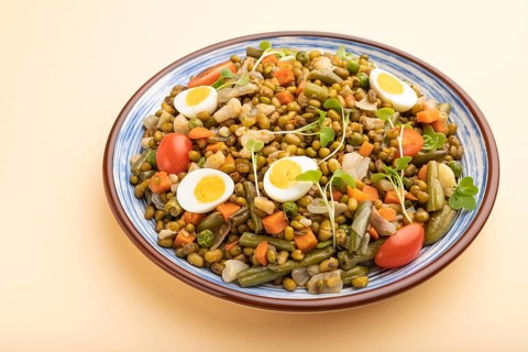 Mung bean porridge with quail eggs, tomatoes and microgreen sprouts on a pastel orange background.