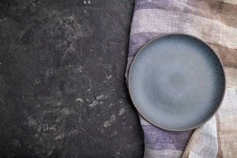 Empty blue ceramic plate on black concrete background and linen textile. Top view, copy space, flat