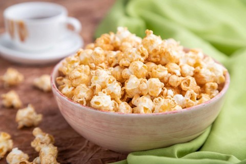 Popcorn with caramel in ceramic bowl on brown concrete background and green textile. Side view,