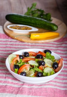 Vegetarian salad of tomatoes, cucumbers, parsley, olives and mustard on linen tablecloth, close up,