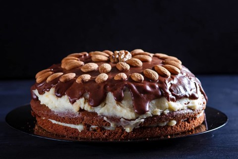 Homemade chocolate cake with milk cream and almonds on black wooden background. close up