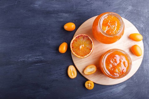 Orange and kumquat jam in a glass jar with fresh fruits on black wooden background. Homemade, top