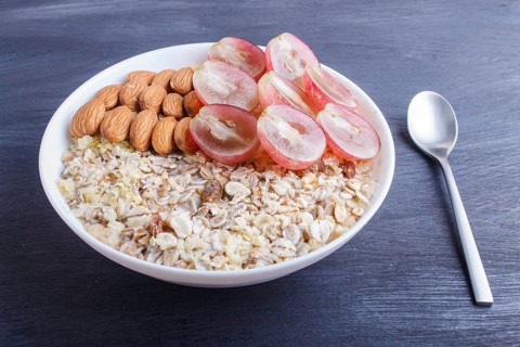 A plate with muesli, almonds, pink grapes on a black wooden background. close up