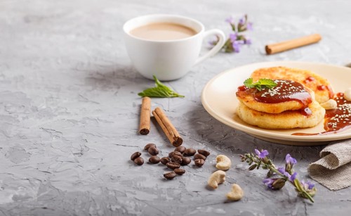 Cheese pancakes with caramel sauce on a beige ceramic plate and a cup of coffee on a gray concrete
