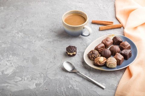 Different chocolate candies and a cup of coffee on a gray concrete background and orange textile.