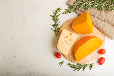 Various types of cheese with rosemary and tomatoes on wooden board on a white wooden background and