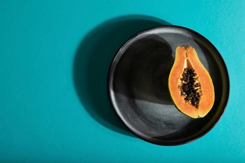 Ripe cut papaya on gray plate on blue pastel background. Top view, flat lay, copy space, hard light