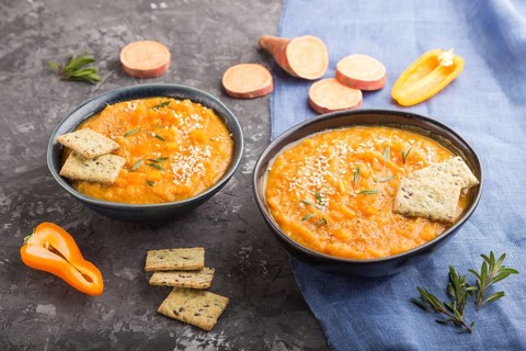 Sweet potato or batata cream soup with sesame seeds and snacks in blue ceramic bowls on a black
