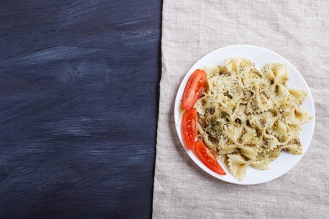 Farfalle pasta with pesto sauce, tomatoes and cheese on a linen tablecloth on black wooden