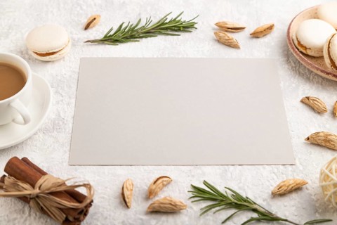 Gray paper sheet mockup with cup of coffee, almonds and macaroons on gray concrete background.