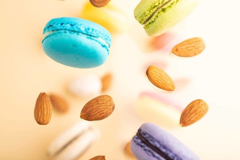 Multicolored flying macaroons and almonds frozen in the air on blurred beige background. top view,