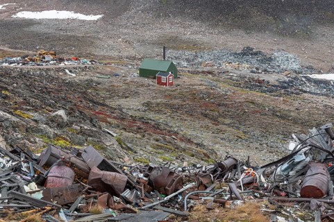 Cabin near scrap yard in rocky, hilly landscape with snow remains, arctic settlement